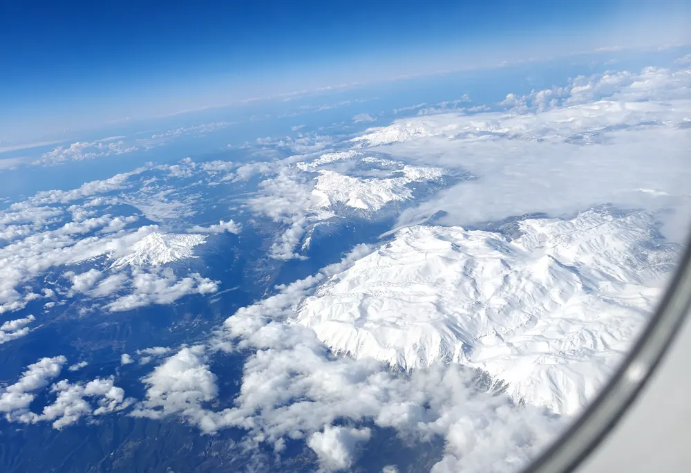 Snow-covered mountain ranges seen through an aircraft window above the clouds