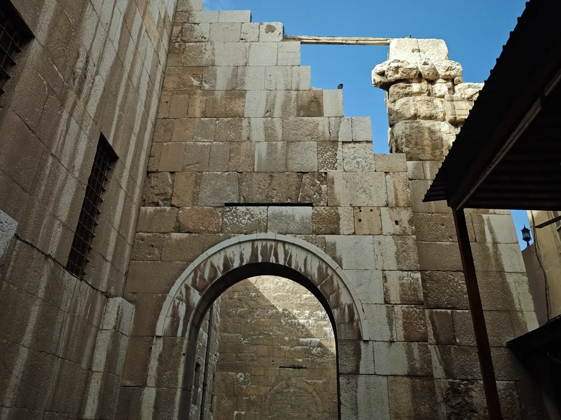 A weathered stone arch and masonry in an old city, against a clear sky