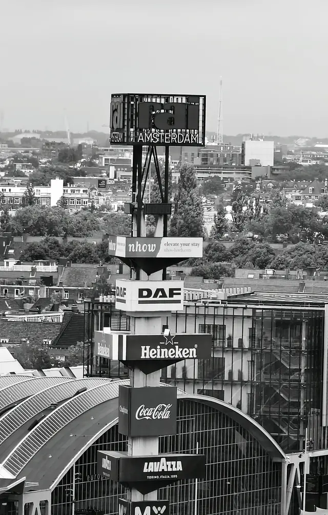 A tall signal mast above exhibition halls, with advertising boards below it, in black and white
