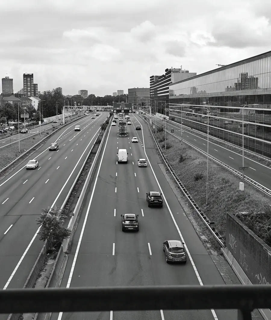 An elevated view over a multi-lane motorway carrying light traffic, in black and white