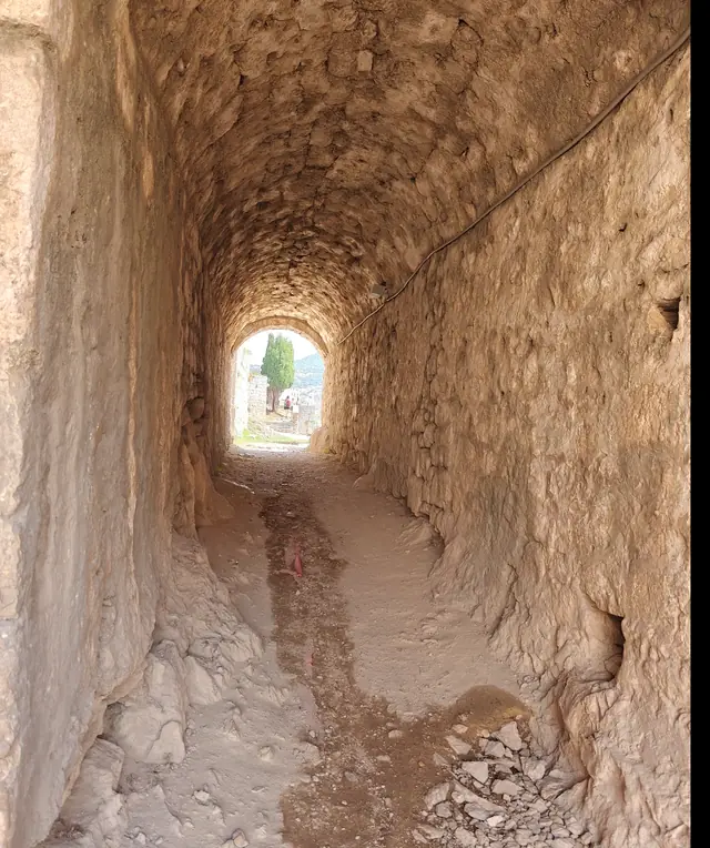 The curved stone wall of a lit passage tunnel